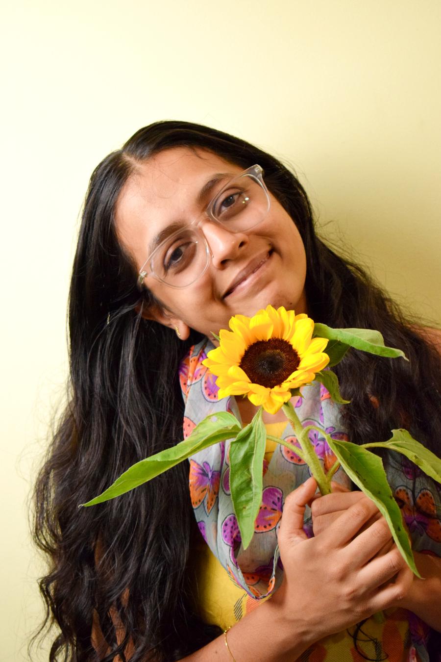 Sneha, founder of The Tempt Bakehouse, smiling with a sunflower